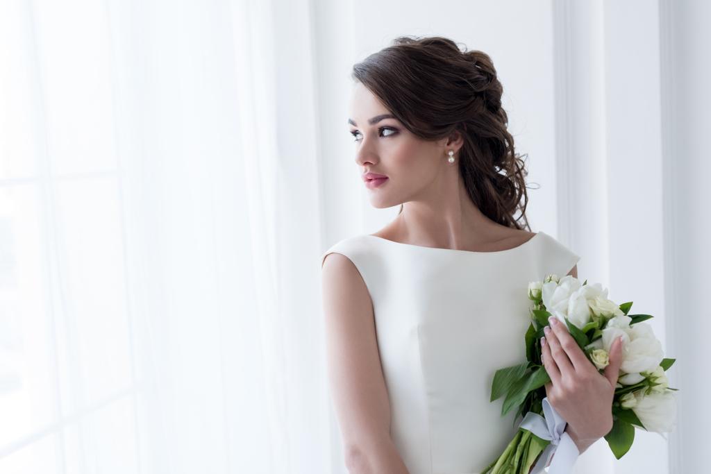 красивая невеста держит свадебный букет и смотрит в окно
 - Фото, изображение