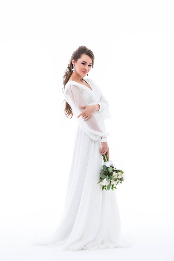 Lächelnde Braut posiert in weißem Kleid mit Brautstrauß, isoliert auf weiß - Foto, Bild