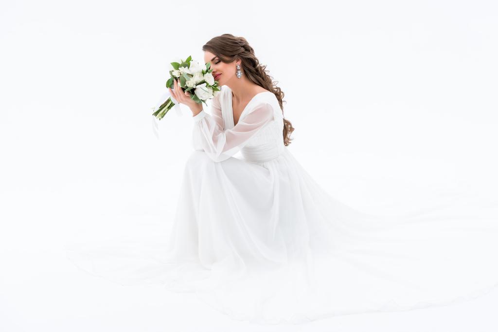 happy bride in traditional dress sniffing wedding bouquet, isolated on white - Photo, Image