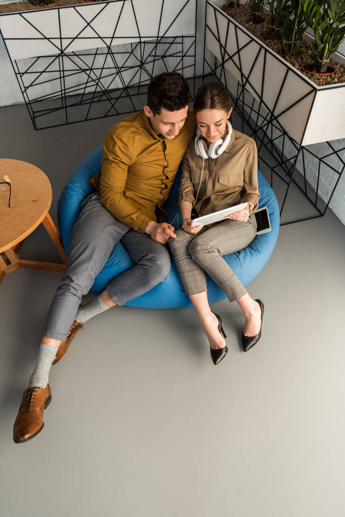 высокий угол зрения молодой пары с помощью планшета вместе, сидя в бобовом мешке
 - Фото, изображение