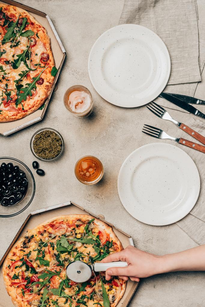 Nahaufnahme einer Frau beim Pizza schneiden auf hellem Hintergrund - Foto, Bild