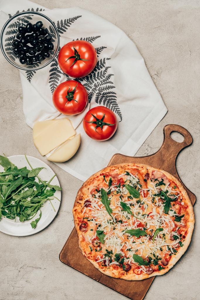 Deliziosa pizza su tagliere in legno e ingredienti per ricette su sfondo chiaro
 - Foto, immagini