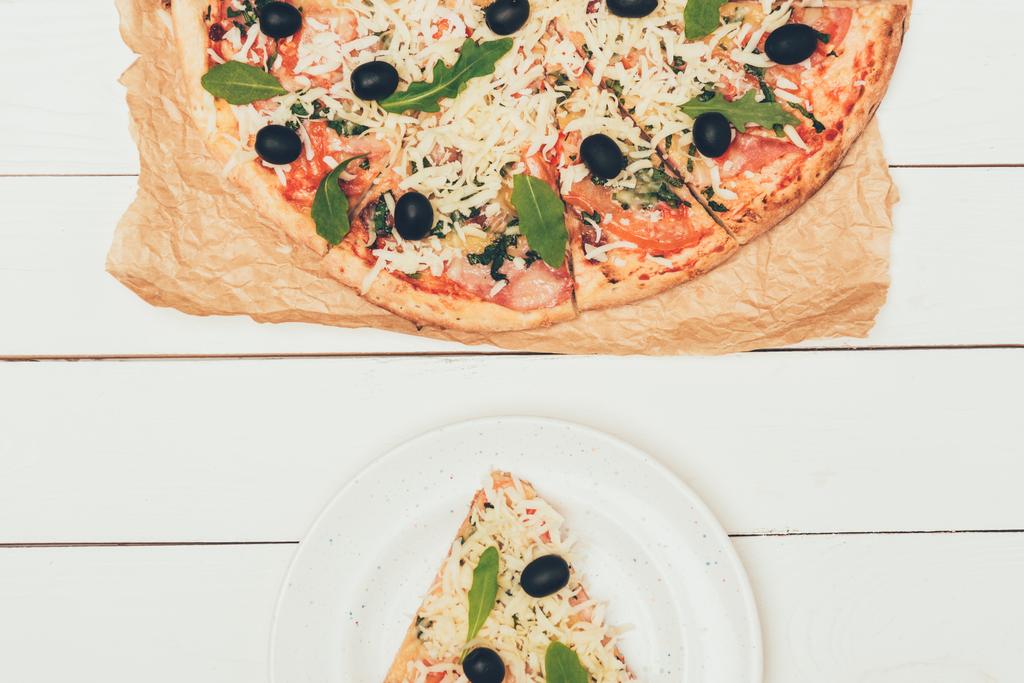 Pizza-Scheibe und ganze Pizza auf weißem Holzgrund - Foto, Bild