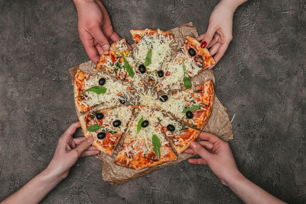 Detailní pohled lidí ruce, přičemž pizza plátky na tmavém pozadí - Fotografie, Obrázek