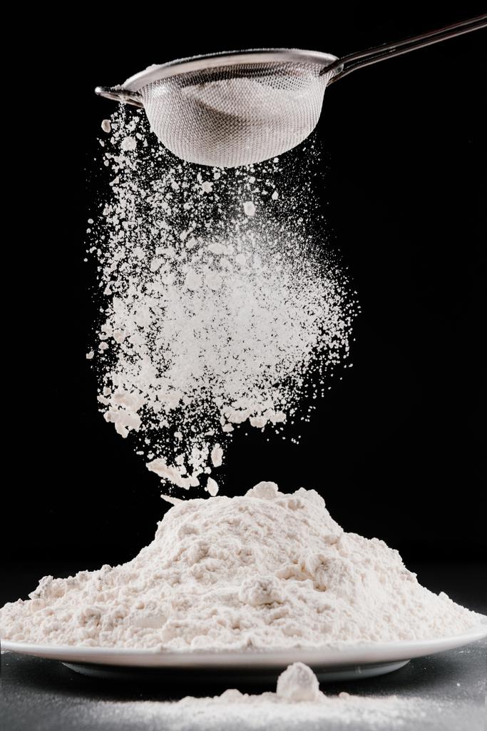 Mehl fällt aus Sieb auf Stapel, isoliert auf schwarz - Foto, Bild