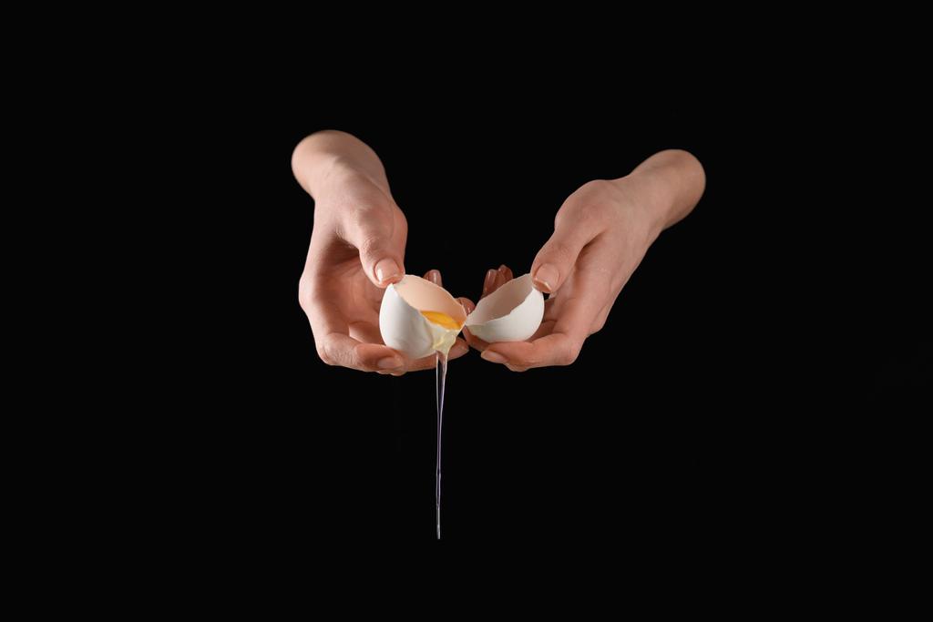 imagen recortada de mujer sosteniendo huevo de gallina goteando roto aislado en negro
 - Foto, Imagen