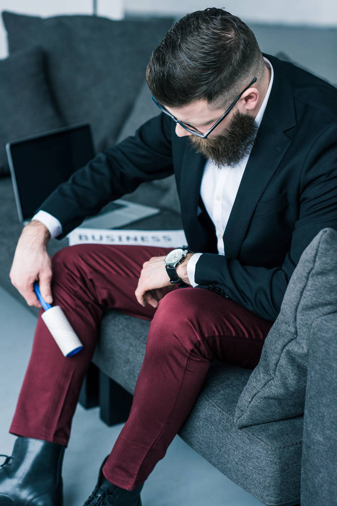 pantaloni uomo d'affari pulizia con pennello appiccicoso mentre seduto sul divano
 - Foto, immagini
