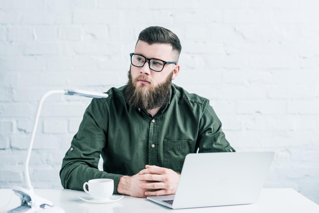portrét promyšlené podnikatel sedí na pracovišti s šálkem kávy a laptop - Fotografie, Obrázek
