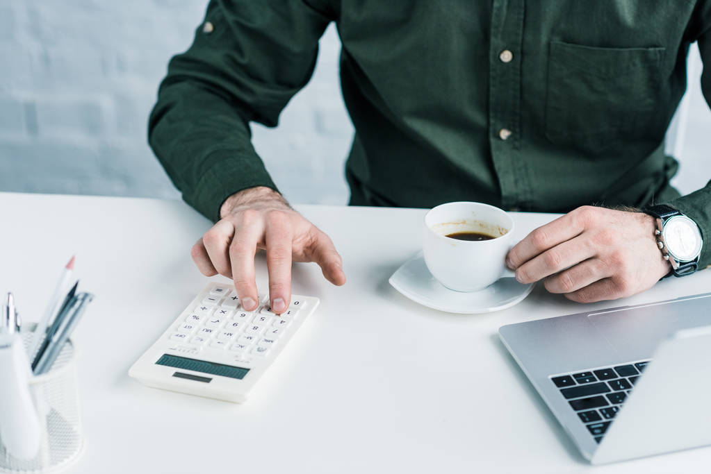 Μερική άποψη του επιχειρηματία κάνοντας υπολογισμούς στο χώρο εργασίας με φλιτζάνι καφέ - Φωτογραφία, εικόνα