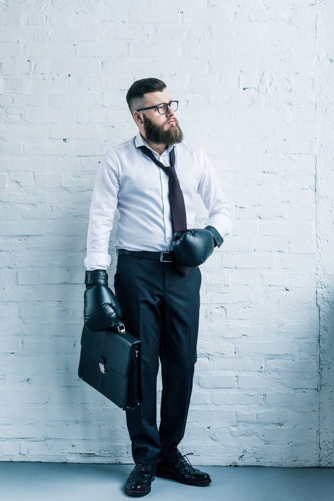 homme d'affaires barbu en gants de boxe tenant une valise contre un mur de briques blanches
 - Photo, image