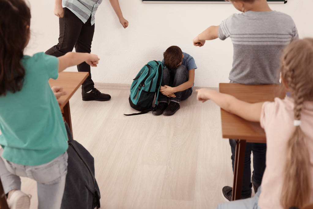 教室の床の上に座っていじめられた少年 - 写真・画像