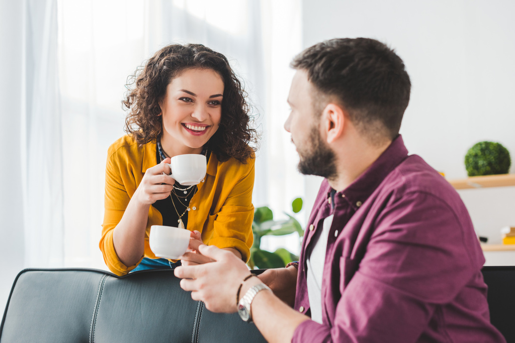Женщина держит кофейные чашки во время разговора с парнем
 - Фото, изображение