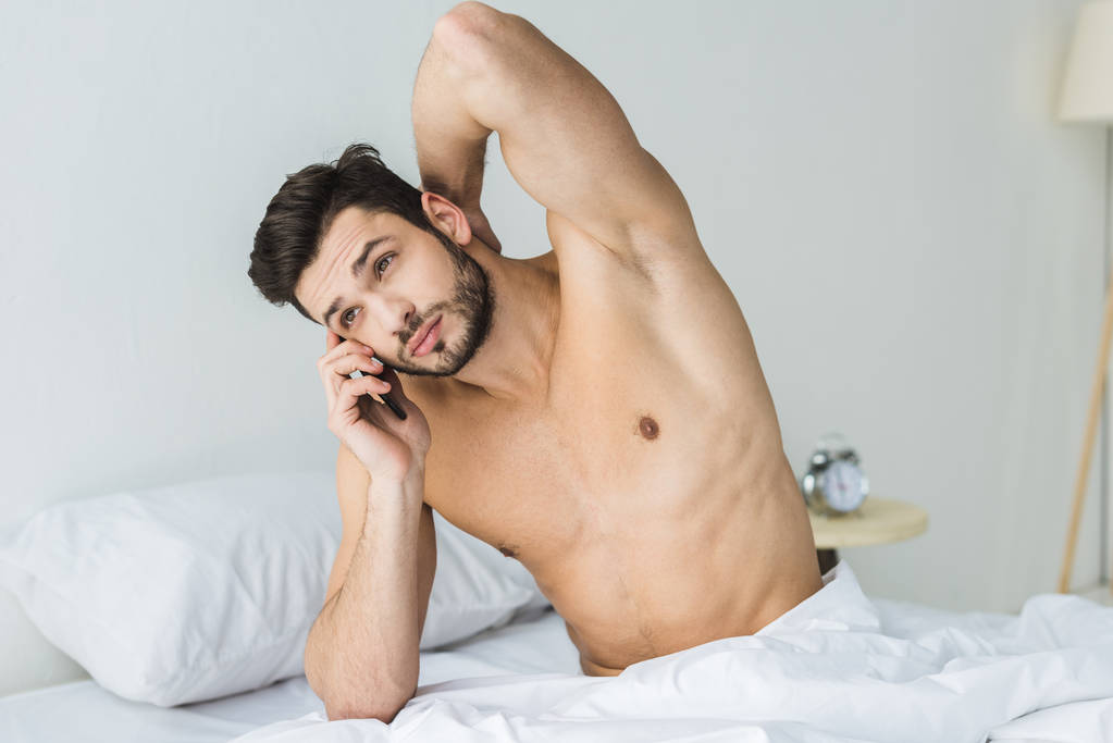 όμορφος άνδρας shirtless μιλώντας στο smartphone στο κρεβάτι το πρωί - Φωτογραφία, εικόνα