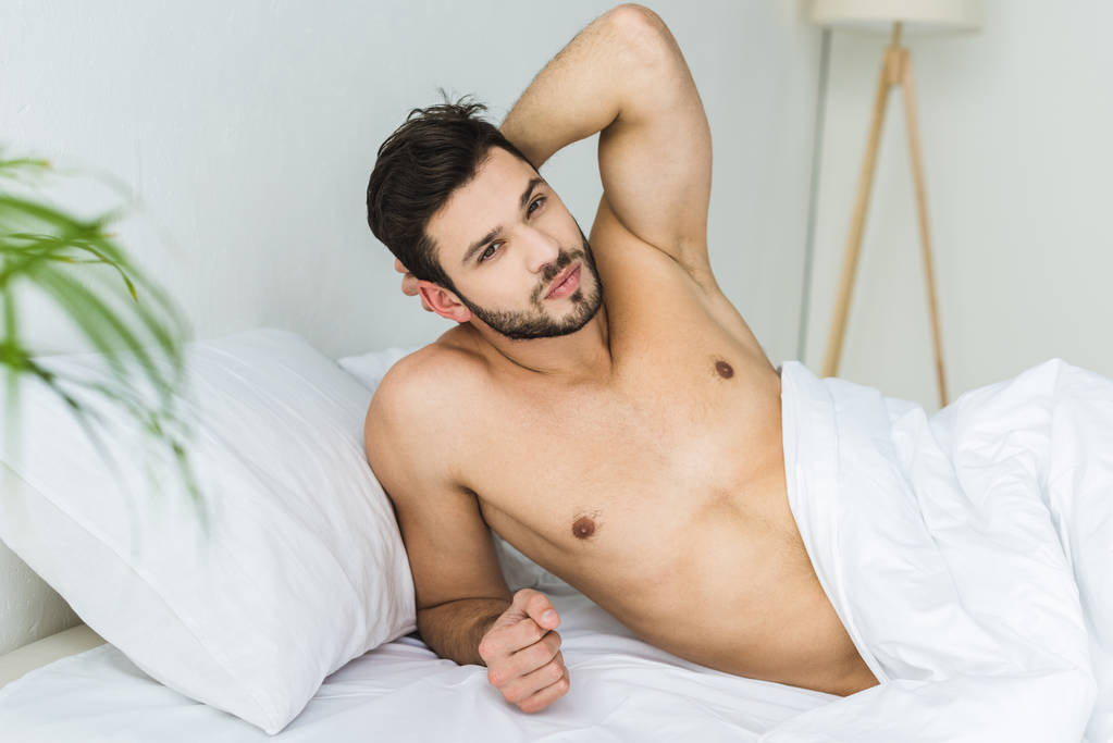 knappe shirtless man ontspannen in witte bed - Foto, afbeelding