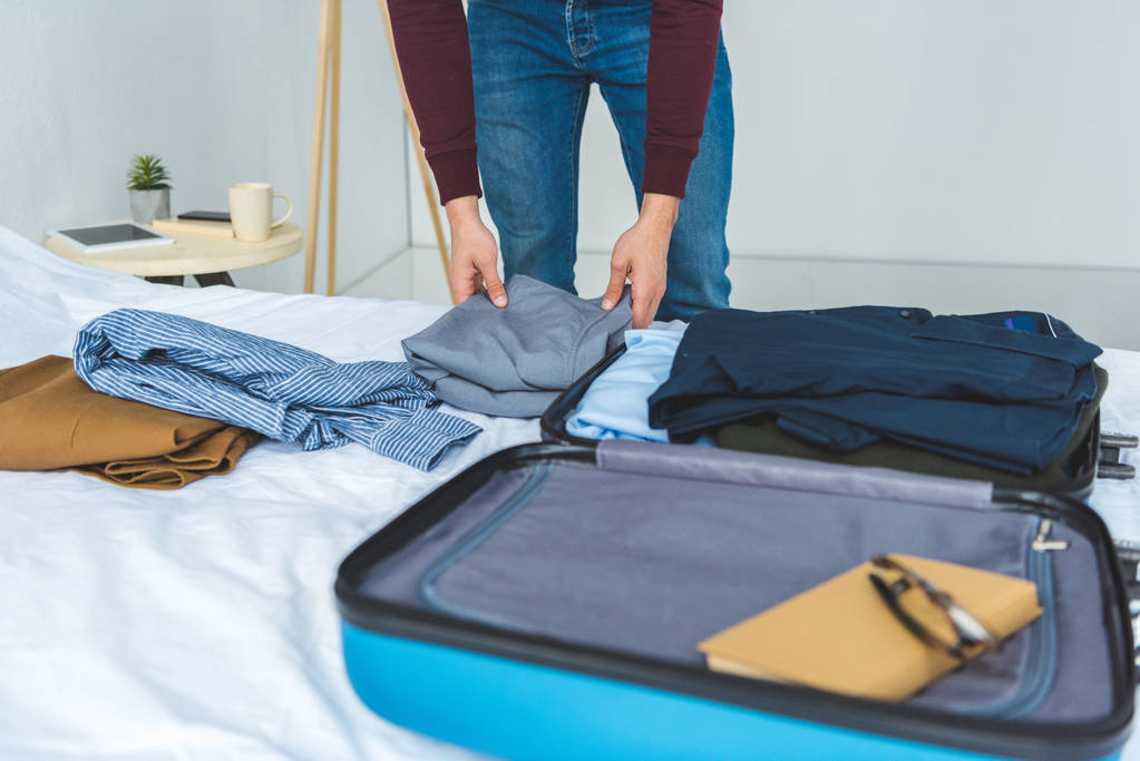 vista recortada del hombre embalaje de ropa en la bolsa de viaje en la cama
  - Foto, imagen