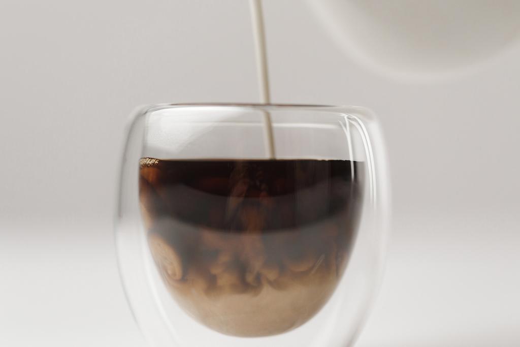 Verter leche en taza con café sobre fondo blanco
 - Foto, Imagen