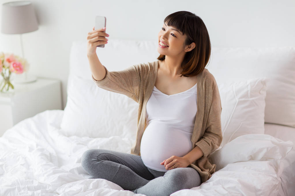 raskaana oleva nainen ottaa selfie älypuhelimella kotona
 - Valokuva, kuva