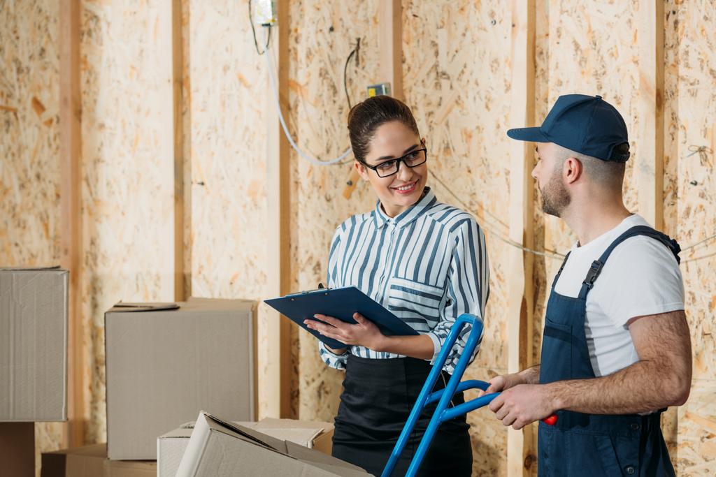 Delivery man and businesswoman filling checklist by stacks of boxes - Photo, Image