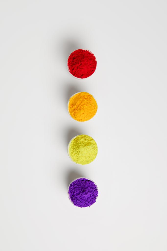 bovenaanzicht van kleurrijke holi verf in kommen in rij op wit - Foto, afbeelding