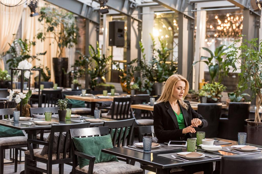 красива жінка сидить за столом і перевіряє час в кафе
 - Фото, зображення