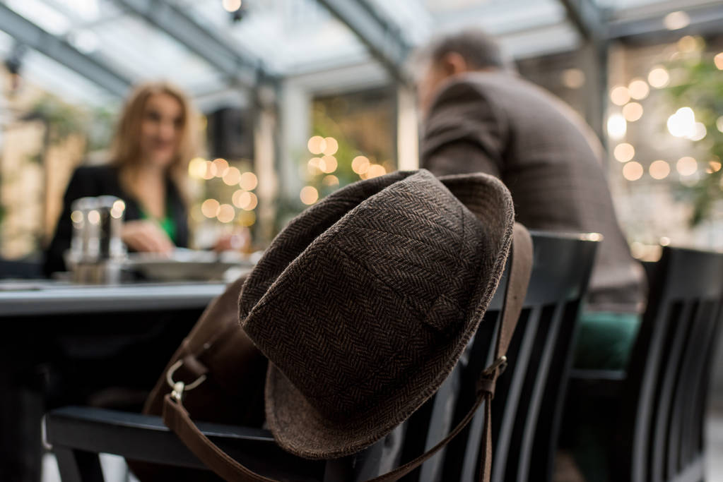 Selektywny fokus kapelusz na krzesło i para przy stoliku w kawiarni - Zdjęcie, obraz
