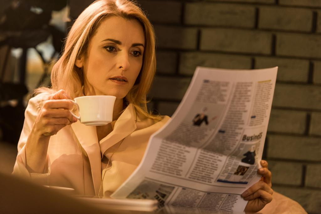 portrait of focused businesswoman with cup of coffee reading newspaper in cafe - Photo, Image