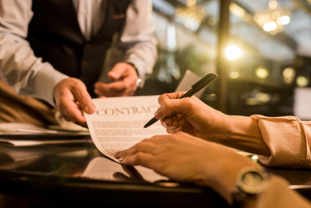 обрезанный снимок подписания контракта предпринимательницей во время встречи с коллегой по бизнесу в кафе
 - Фото, изображение