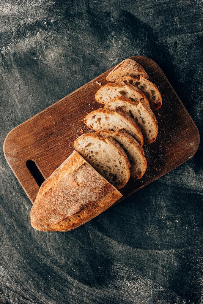 pohled shora uspořádány kousky chleba na prkénku na tmavý povrch s moukou - Fotografie, Obrázek
