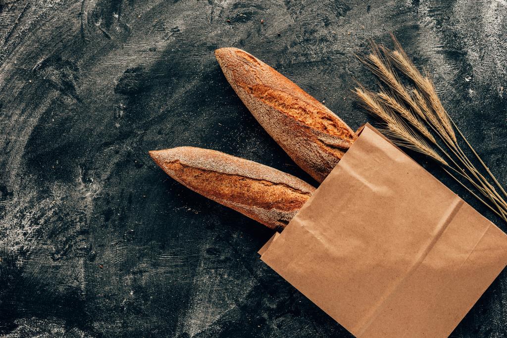 vista superior de las baguettes francesas dispuestas en bolsa de papel y trigo sobre mesa oscura con harina
 - Foto, Imagen