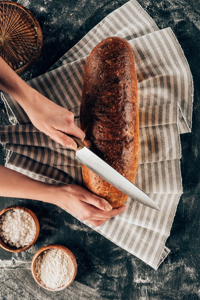 colpo ritagliato di donna che taglia la pagnotta di pane su lino su tavolo scuro con farina
 - Foto, immagini