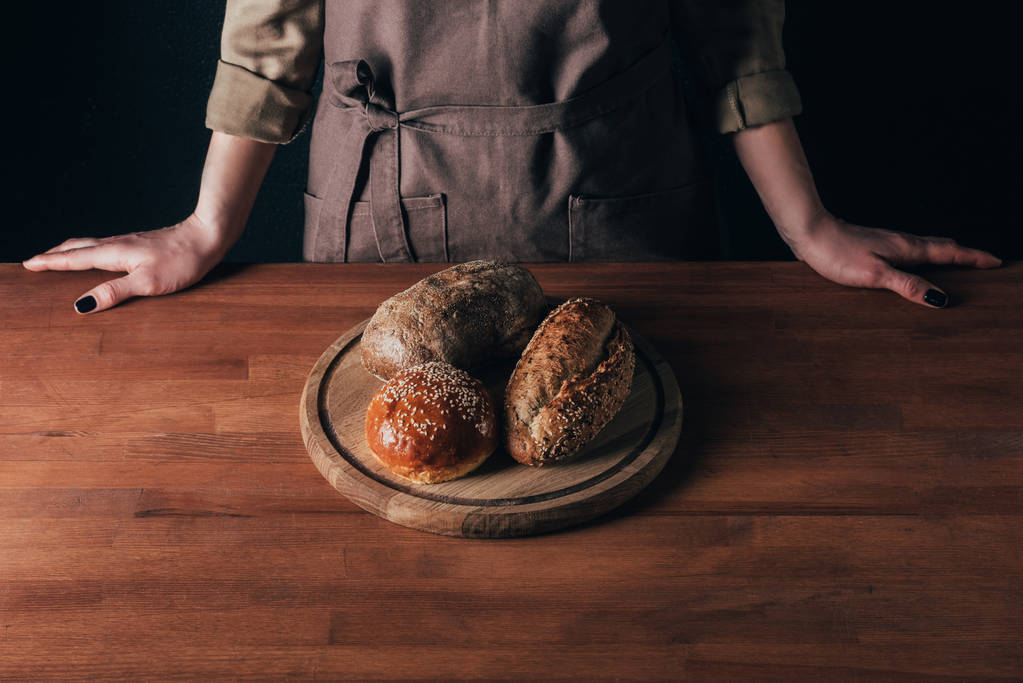 ekmek ahşap kesme tahtası üzerinde kısmi ile masada duran kadın görünümünü loafs - Fotoğraf, Görsel