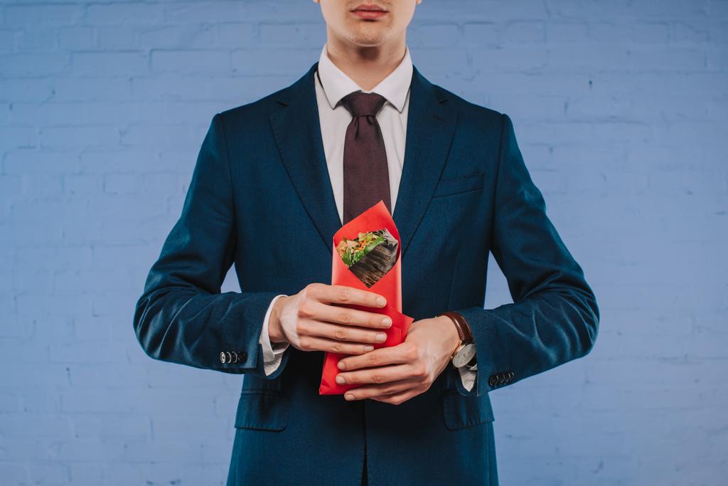 Schnappschuss eines jungen Geschäftsmannes im Anzug, der einen mit rotem Papier bedeckten Döner hält - Foto, Bild