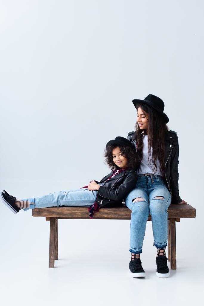 moeder en dochter in soortgelijke kleding, zittend op de Bank samen geïsoleerd op grijs - Foto, afbeelding