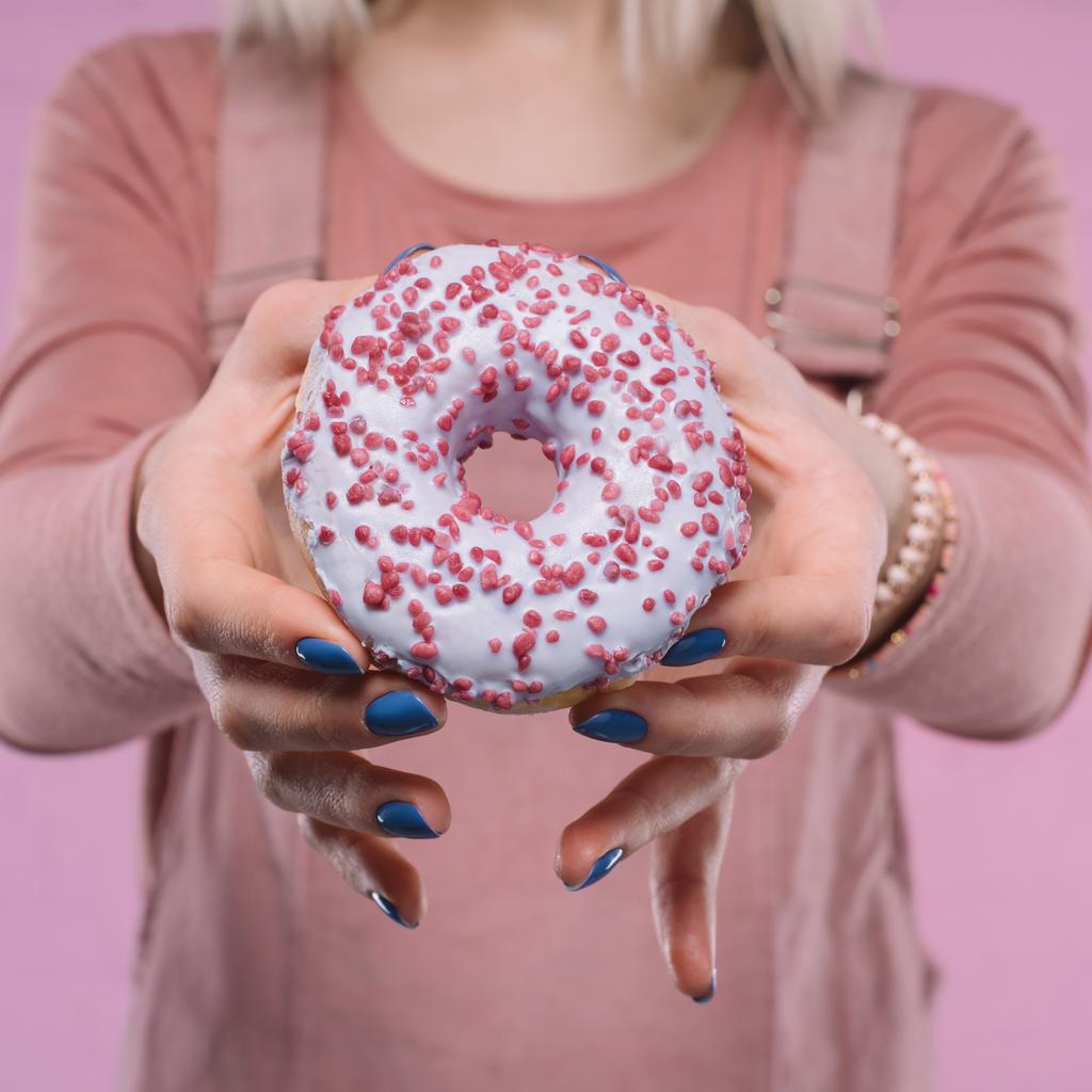 обрезанный снимок женщины, показывающей вкусный глазированный пончик на камеру
 - Фото, изображение