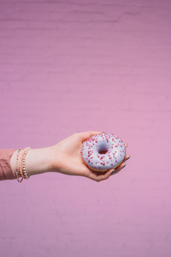 Schnappschuss einer Frau mit glasiertem Donut in der Hand vor rosa Ziegelwand - Foto, Bild