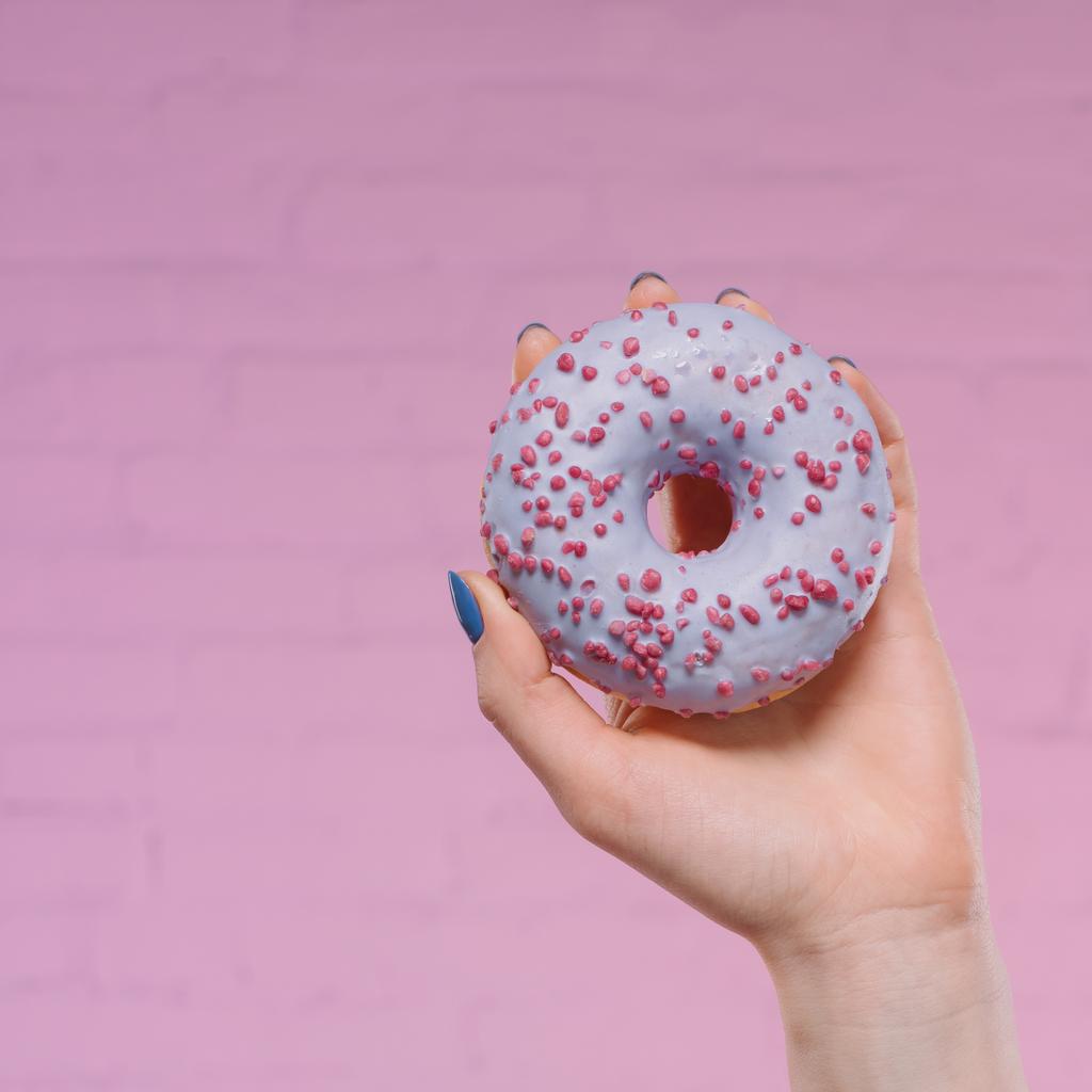 Schnappschuss einer Frau mit süßem glasiertem Donut in der Hand vor rosa Ziegelwand - Foto, Bild
