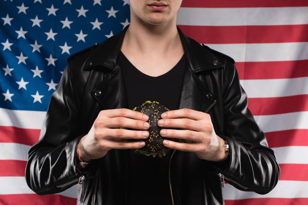 vágott lövés a fiatal férfi bőrkabát fekete burger gazdaság ellen usa zászló - Fotó, kép