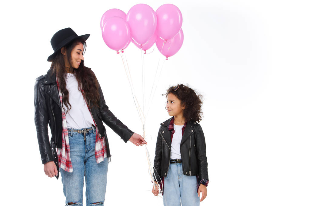Gelukkig moeder en dochter in soortgelijke kleren met roze ballonnen geïsoleerd op wit - Foto, afbeelding