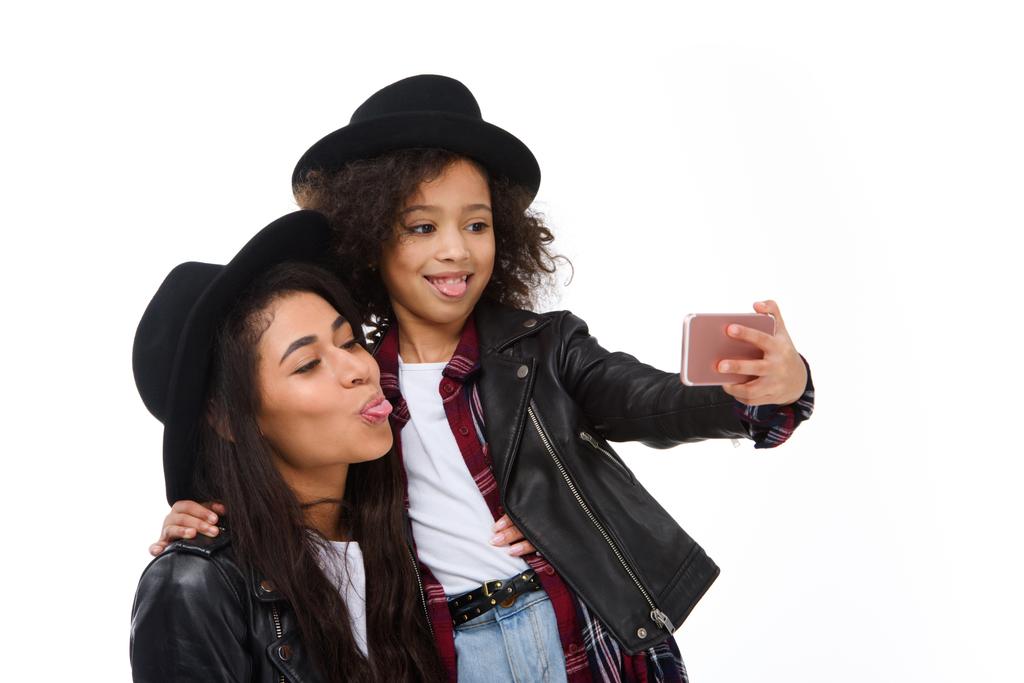 stylish mother and daughter taking selfie with smartphone and grimacing isolated on white - Photo, Image