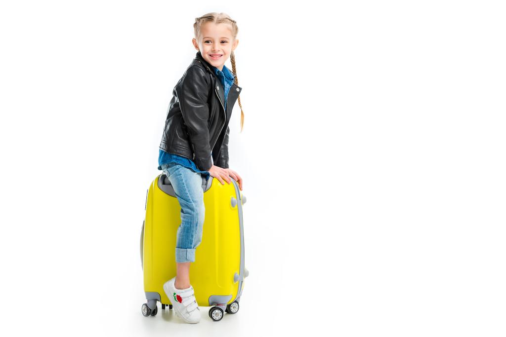 Lachende weinig toeristische zittend op gele wiel koffer geïsoleerd op wit - Foto, afbeelding