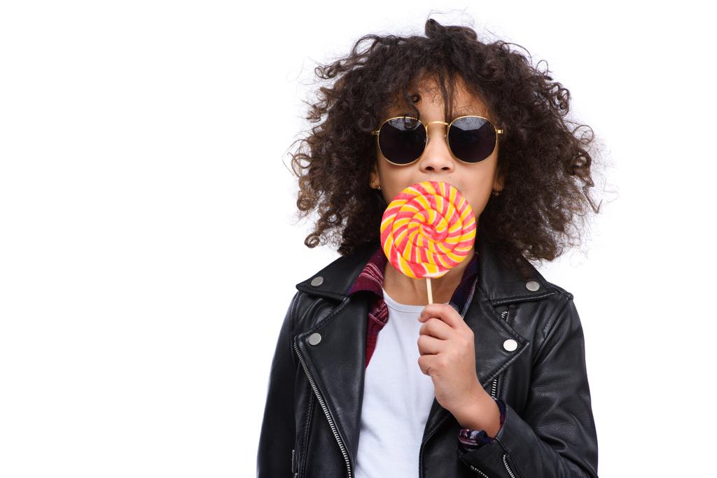 linda criança em jaqueta de couro e óculos de sol comendo pirulito isolado no branco
 - Foto, Imagem