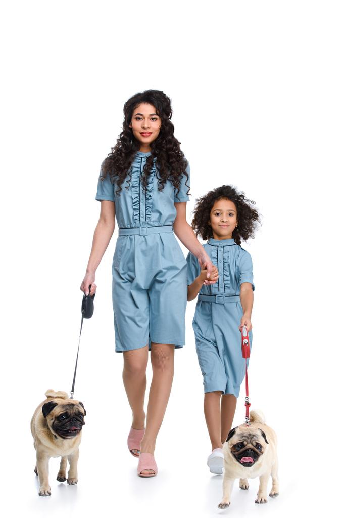 beautiful mother and daughter in similar dresses walking with pugs isolated on white - Photo, Image