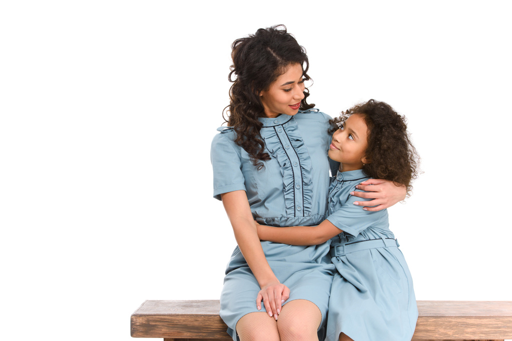 μητέρα και κόρη αγκαλιάζει ενώ κάθεται σε παγκάκι απομονωθεί σε λευκό - Φωτογραφία, εικόνα