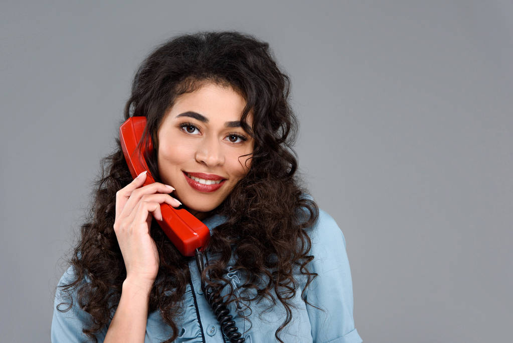 Gelukkig jonge vrouw praten door vintage rode telefoon geïsoleerd op grijs - Foto, afbeelding