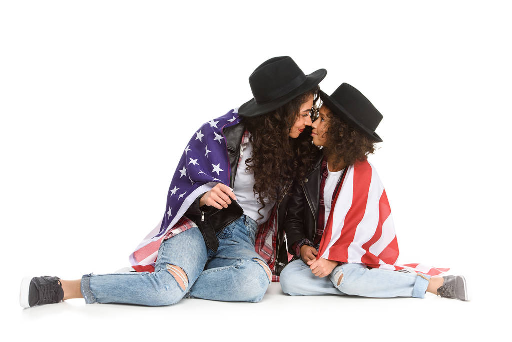 красива мати і дочка вкриті прапором США, сидячи на підлозі ізольовані на білому
 - Фото, зображення