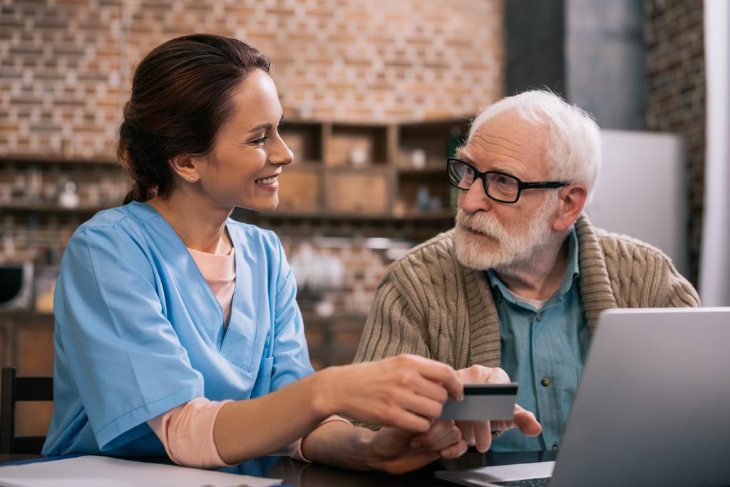 Krankenschwester hilft Seniorin mit Laptop und Kreditkarte - Foto, Bild