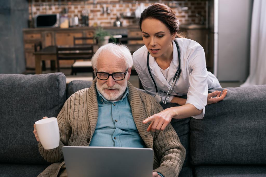 Arzt zeigt auf Laptop in den Händen eines älteren Patienten - Foto, Bild