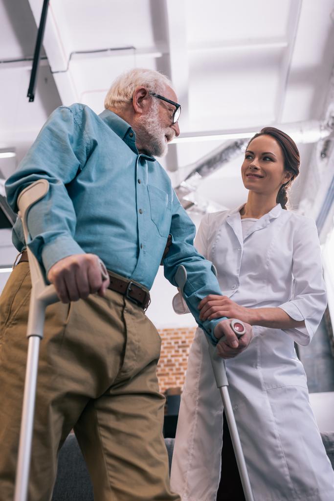 Uomo anziano appoggiato alle stampelle e sorridente medico femminile
 - Foto, immagini