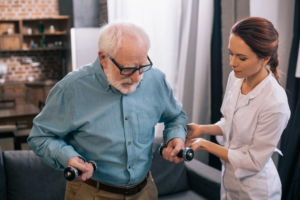 Medico donna e uomo anziano con manubri durante la fisioterapia
 - Foto, immagini