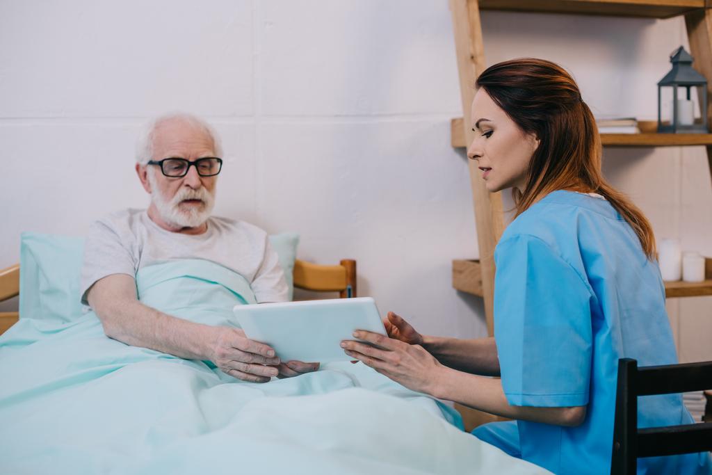 Paziente anziano e caregiver utilizzando tablet
 - Foto, immagini